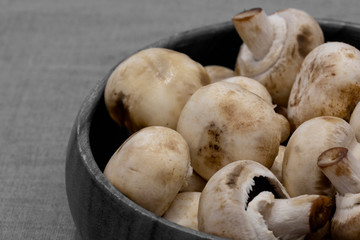 Closed cup white mushrooms in a wooden bowl.  On a grey tablecloth with selective colour
