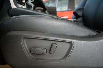 the seat level adjust button beside the grey  leather seat in the car