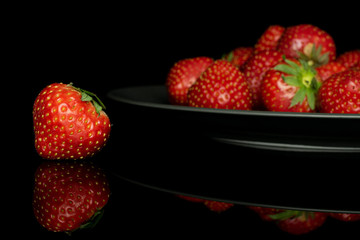 Lot of whole fresh red strawberry on gray ceramic plate isolated on black glass