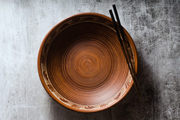 empty clay plate and chopsticks on a dark stone background. linen napkin