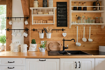 Interior of kitchen in rustic style with vintage kitchen ware and wooden wall. White furniture and wooden decor in bright  cottage indoor. - obrazy, fototapety, plakaty