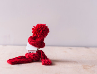 Close up conceptual miniature model house with red wool scarf hat on wooden background.