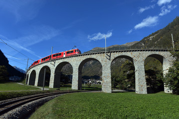 Swiss mountain train Bernina Express passes the spiral of the Brusio Viaduct