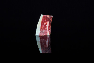 studio shot of a slice of 100% Iberian acorn-fed ham on a black background with the reflection