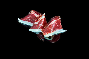 studio photo of a series of slices of 100% Iberian acorn-fed ham folded on black background with...