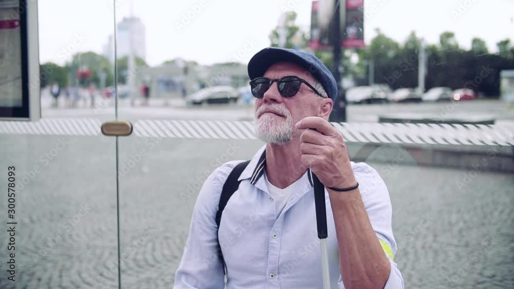 Wall mural Senior blind man with white cane waiting at bus stop in city.