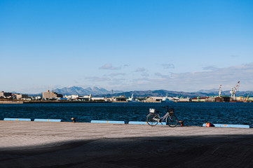 Fototapeta na wymiar DEC 1, 2018 Hakkodate, Japan - Hakkodate port pier with bicycle in bright winter sun blue sea cityscape in background.