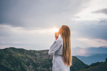 Woman in SPA bathrobe standing back in the beautiful mountain view at the sunset. Travel and healthy lifestyle and beauty outdoors. - obrazy, fototapety, plakaty