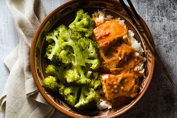 Thai salmon dish in coconut sauce with fresh broccoli and rice in a clay bowl with chopsticks . healthy food with vitamin B5...