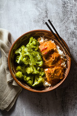 Thai salmon dish in coconut sauce with fresh broccoli and rice in a clay bowl with chopsticks . healthy food with vitamin B5...