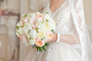 Beautiful wedding bouquet of roses, peonies with ribbons and lace in the hands of the bride, wedding details