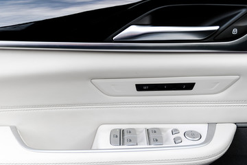 Fototapeta premium Door handle with power window control buttons of a luxury passenger car. White perforated leather interior with stitching and natural wood panel. Modern car interior details. Car detailing. Car inside