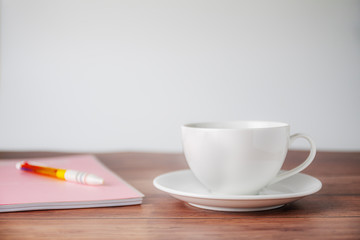 A cup of coffee with notebook on wooden background