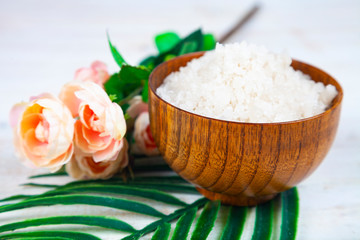 Wooden bowl with sea salt, rose and palm leaf.