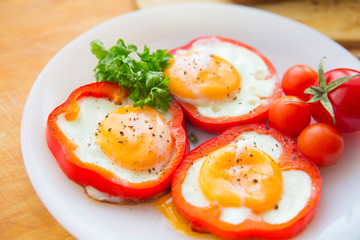 Fried eggs in red peppers. Fried eggs in paprika served on white plate on wooden background