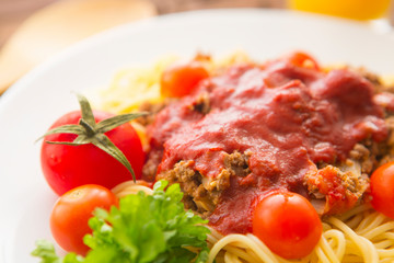 Bowl of spaghetti bolognese with tomatoes on wooden table in background