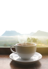 White ceramic coffee cup on wooden table  in morning with sunlight over blurred mountains landscape 