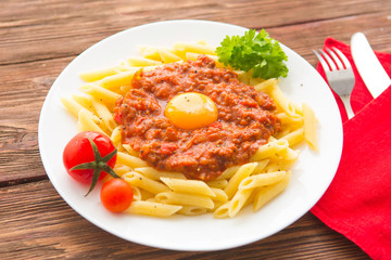 Penne pasta with a bolognese tomato beef sauce on wooden table