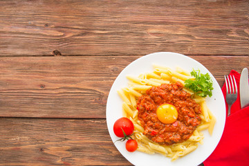 Penne pasta with a bolognese tomato beef sauce on wooden table. Copy space. Horizontal view from above.