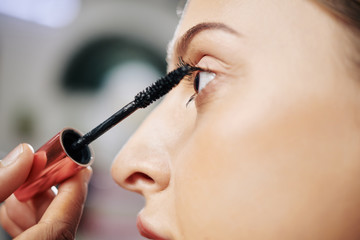 Close-up image of make-up artist applying black voluminous mascara to fashion model before shooting