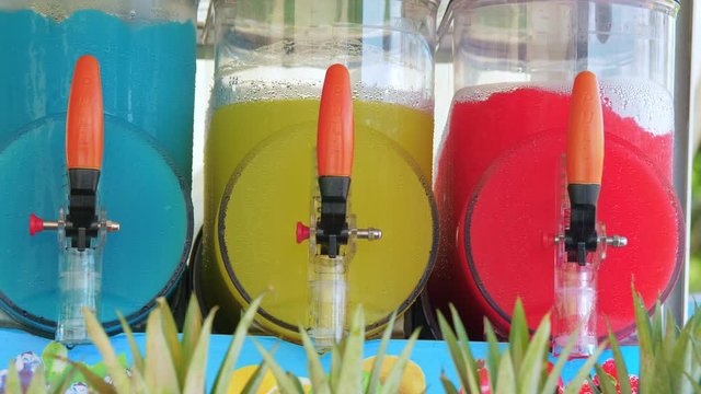 Freezing and mixing machines for making ice slushy drinks containing blue, yellow and red slush. Cold colorful frozen sugar juice.
