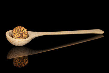 One half of dry brown nutmeg in a wooden spoon isolated on black glass