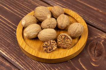 Group of eight whole one half one piece of dry brown nutmeg on bamboo coaster on brown wood