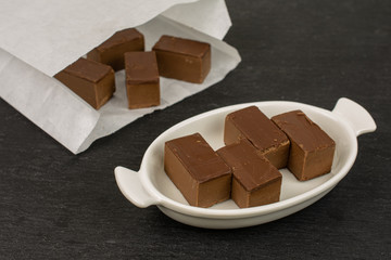 Lot of whole sweet brown viennese nougat in white oval ceramic bowl in paper bag on grey stone