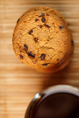 Oatmeal cookies with pieces of chocolate and a mug of coffee on a bamboo stand. Close-up