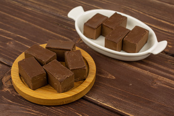 Group of nine whole sweet brown viennese nougat in white oval ceramic bowl on bamboo coaster on brown wood