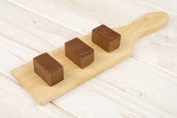 Group of three whole sweet brown viennese nougat on small wooden cutting board on white wood