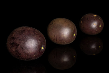 Group of three whole sweet dark purple passion fruit placed diagonally isolated on black glass