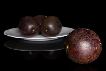 Group of four whole sweet dark purple passion fruit on white ceramic plate isolated on black glass