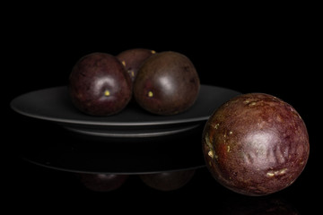Group of four whole sweet dark purple passion fruit on gray ceramic plate isolated on black glass