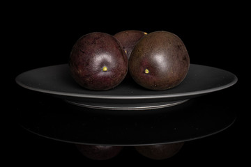 Group of three whole sweet dark purple passion fruit on gray ceramic plate isolated on black glass