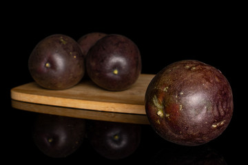 Group of four whole sweet dark purple passion fruit on bamboo cutting board isolated on black glass