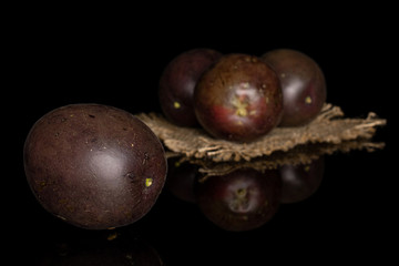 Group of four whole sweet dark purple passion fruit on natural sackcloth isolated on black glass