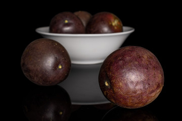 Group of five whole sweet dark purple passion fruit in white ceramic bowl isolated on black glass