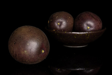 Group of three whole sweet dark purple passion fruit in dark ceramic bowl isolated on black glass