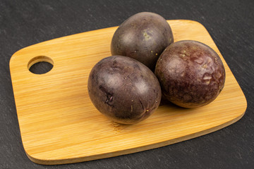 Group of three whole sweet dark purple passion fruit on bamboo cutting board on grey stone