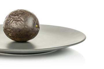 One whole sweet dark purple passion fruit on gray ceramic plate isolated on white background