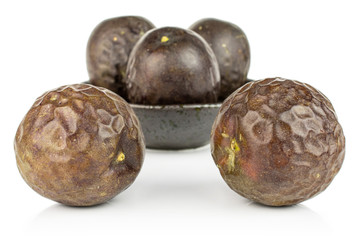 Group of five whole sweet dark purple passion fruit in dark ceramic bowl isolated on white background