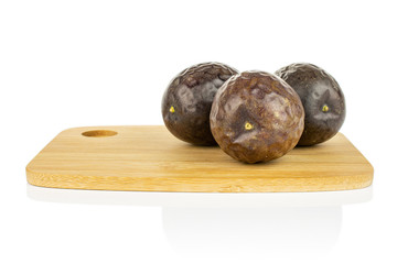 Group of three whole sweet dark purple passion fruit on bamboo cutting board isolated on white background