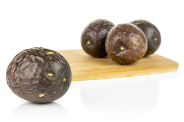 Group of four whole sweet dark purple passion fruit on bamboo cutting board isolated on white background