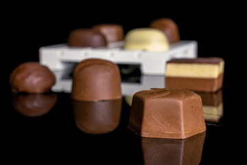 Group of eight whole delicious chocolate praline on white wooden pallet isolated on black glass