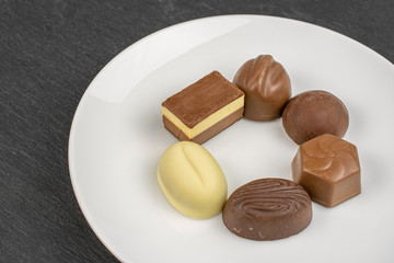 Group of six whole delicious chocolate praline on white ceramic plate on grey stone