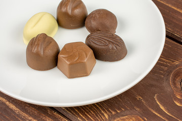Group of six whole delicious chocolate praline on white ceramic plate on brown wood
