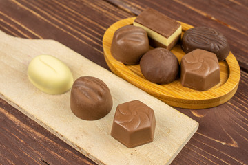 Group of eight whole delicious chocolate praline on bamboo coaster on small wooden cutting board on brown wood