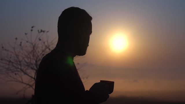 Young bearded guy drinking coffee at dawn. Fragrant coffee in the morning at sunrise. The guy enjoys coffee.The average plan