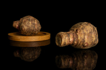 Group of two whole fresh brown jerusalem artichoke on bamboo coaster isolated on black glass